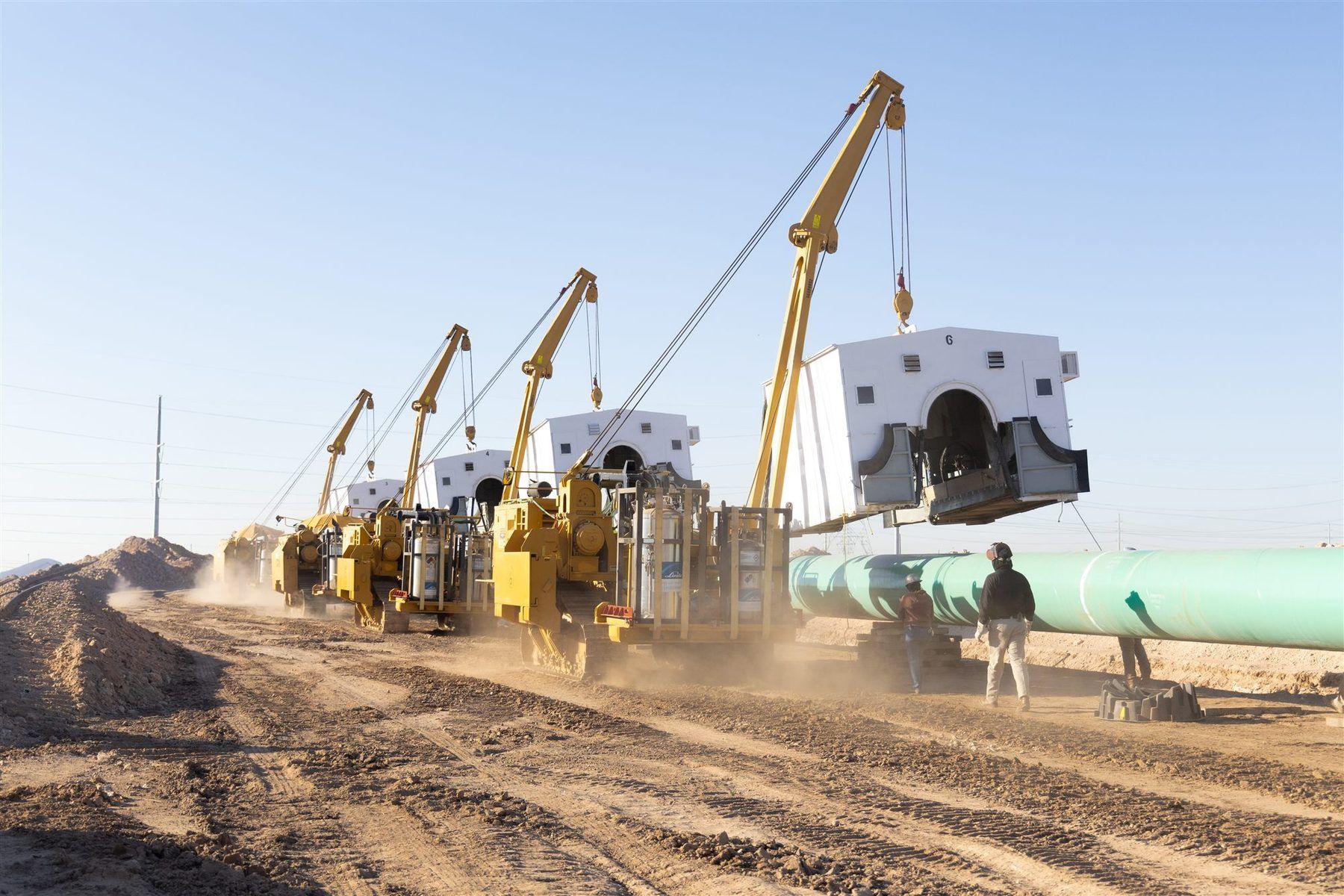 Sidebooms carrying weld shacks along a pipeline firing line on a U.S. right-of-way