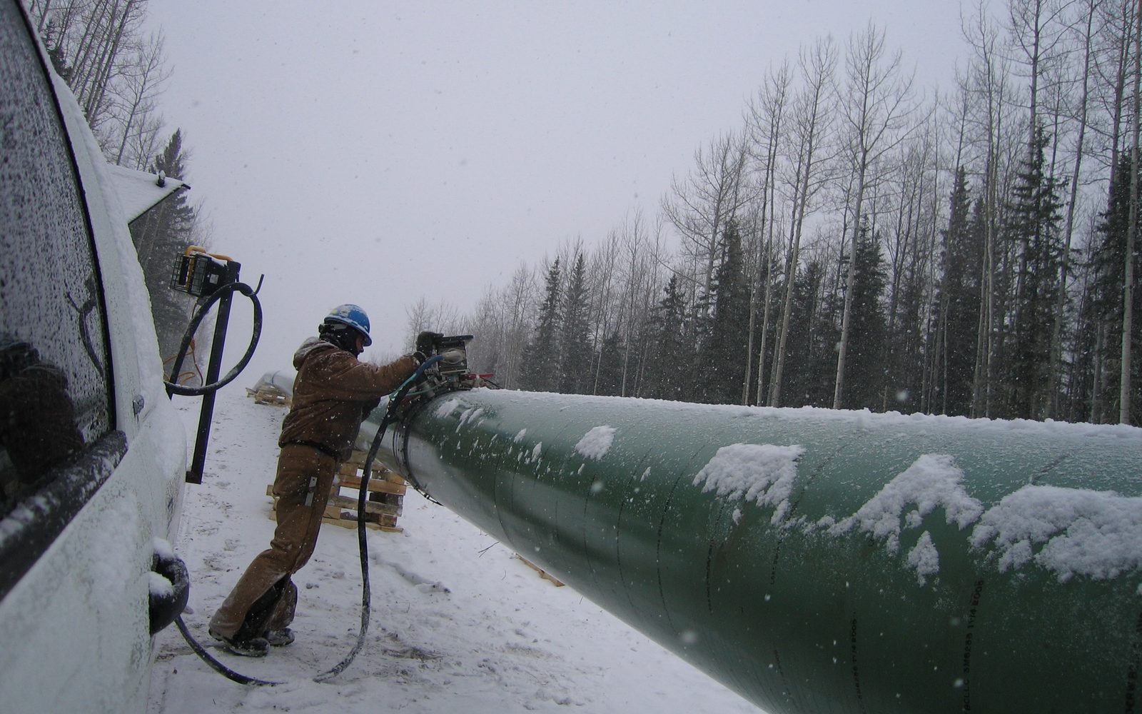 Technician setting an automated ultrasonic scanner on a snow-covered pipeline in the boreal forest